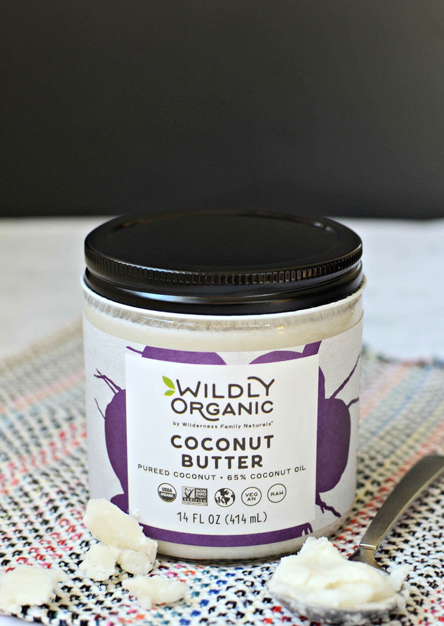 Jar of Wildly Organic Coconut Butter on a patterned cloth, with spoonful nearby