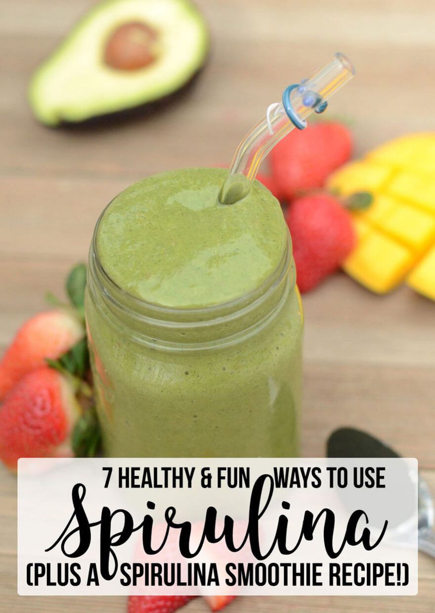 A green spirulina smoothie in a jar with a straw, surrounded by fruits including avocado and strawberries