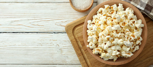 Bowl of popcorn with a side of salt on wood table