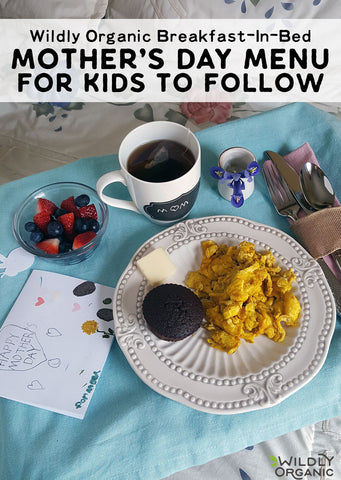 Mother's Day breakfast in bed setup with scrambled eggs, berries, tea, and a handmade card