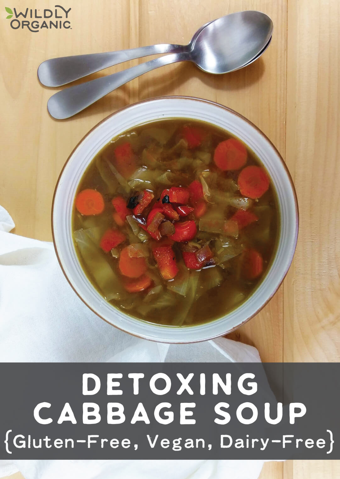 A bowl of detoxing cabbage soup with carrots, red peppers, and cabbage in a light broth, with two spoons placed on the table beside it.