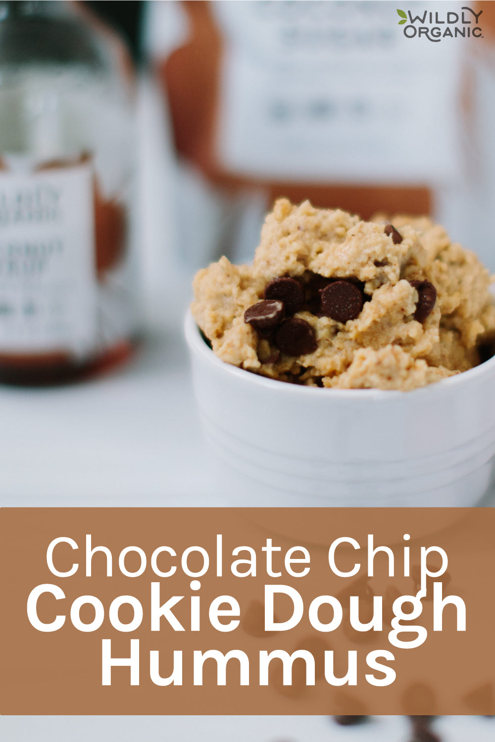 Chocolate chip cookie dough hummus in a white bowl with blurred objects in the background.