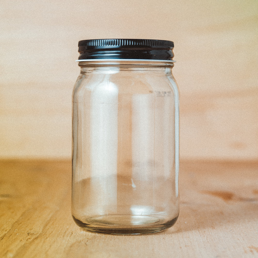 A clear, empty glass jar with a black lid on a wooden surface, ready to be used for storage.