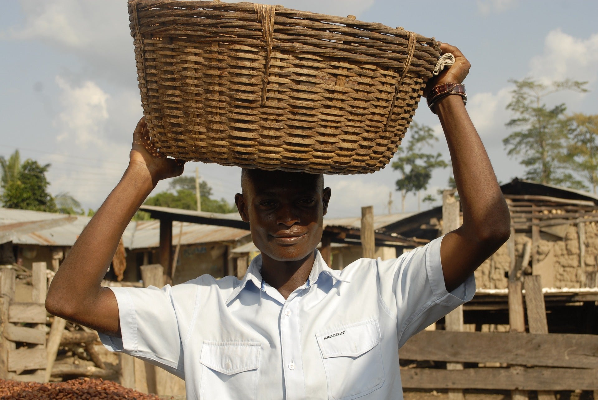 A young African man smiling and holding a wooden basket on top of his head