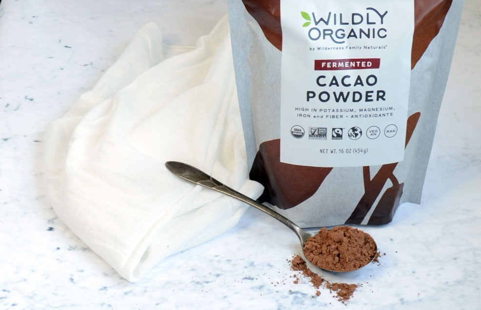 Bag of fermented cacao powder with a spoonful spilled on a marble surface.