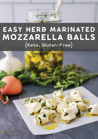 A photo of herb-marinated mozzarella bites on a plate with a jar of olive oil and herbs.