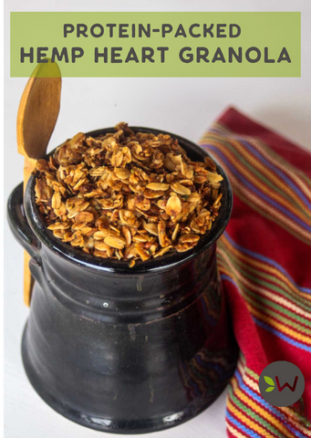 Jar of hemp heart granola on a colorful cloth with a wooden scoop, labeled Protein-Packed.